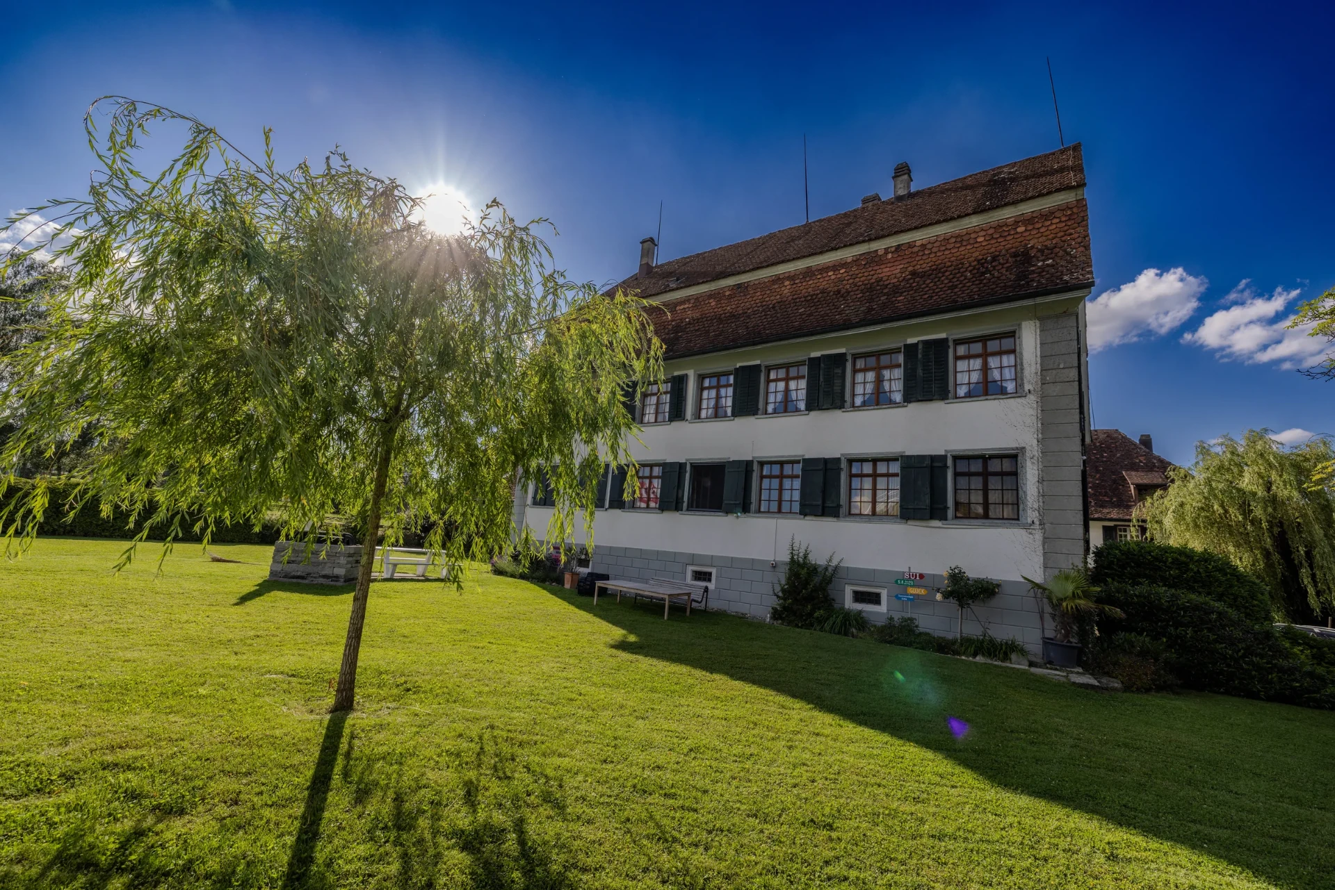 Das historische Schlössli Herrenhof im warmen Abendlicht, umgeben vom Garten